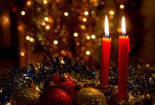 Three red candles with Christmas balls and dark background with lights.