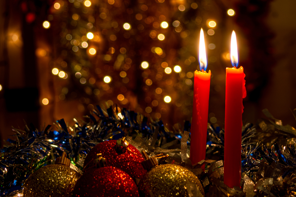 Three red candles with Christmas balls and dark background with lights.