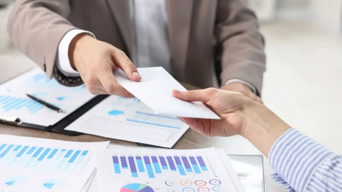 business muži si nad dokumenty předávají obálku