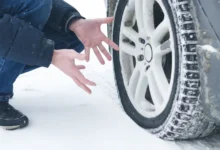 Muž u pneumatiky svého vozu na sněhu