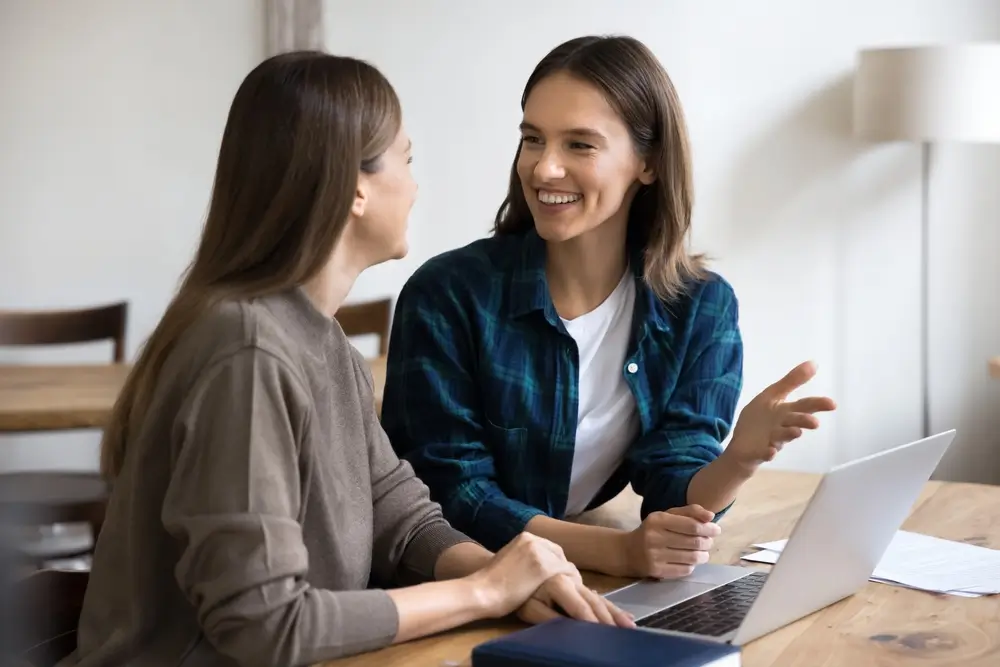 Ženy sedí u notebooku a hovoří spolu.