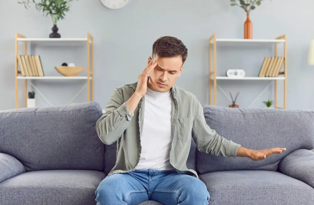 Mladý muž sedí na gauči a drží se za hlavu.
