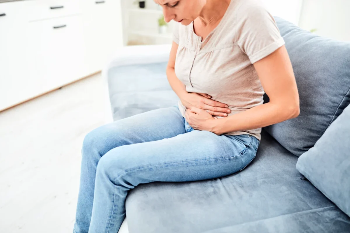 Žena, která sedí na gauči a bolí ji břicho.