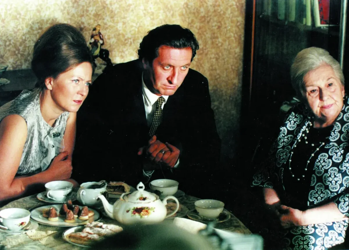 Dvě ženy a jeden muž sedí u stolku s kávou a něco sledují.