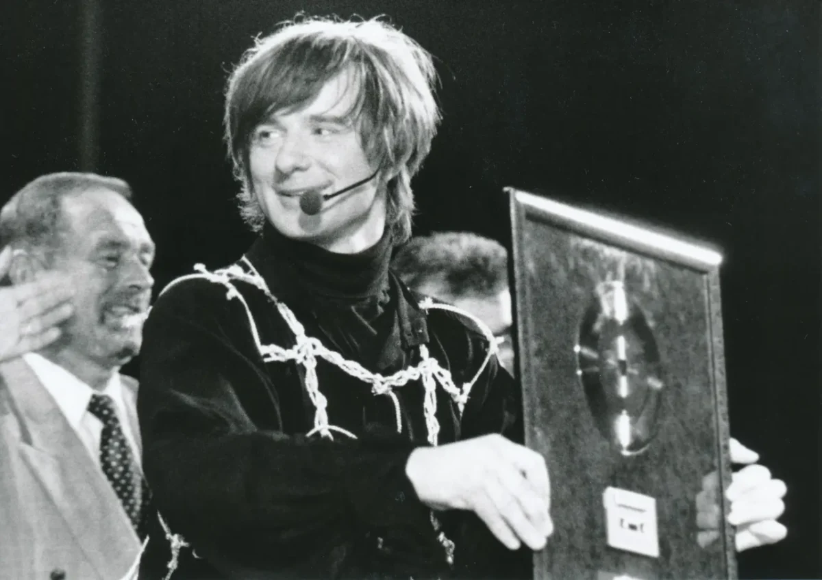 Muž s mikrofonem u pusy drží v ruce desku.