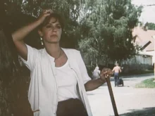 Žena v bílé oblečení se drží jednou rukou za hlavu a v druhé drží násadu.