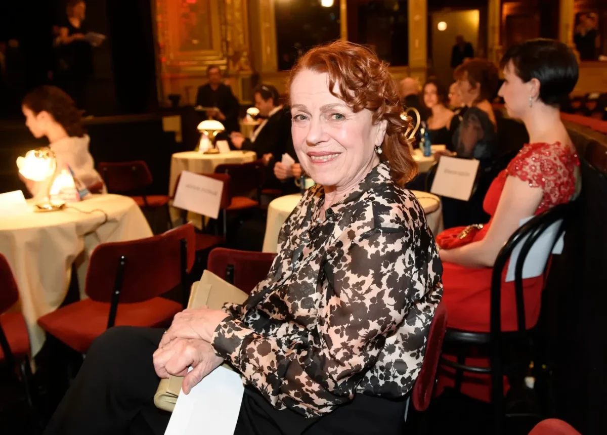 Žena ve společenském oblečení sedí u stolu v místnosti s intimním osvětlením.