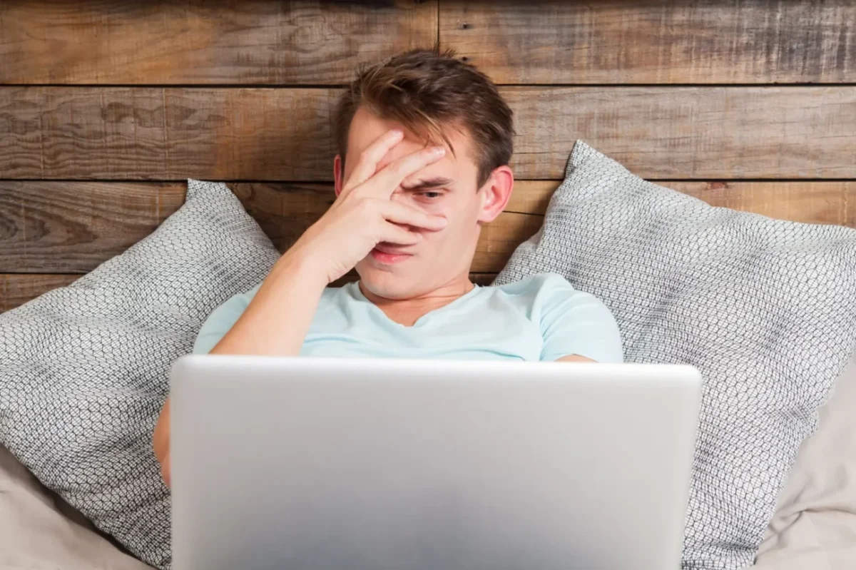 muž skrze prsty sleduje cosi na obrazovce laptopu