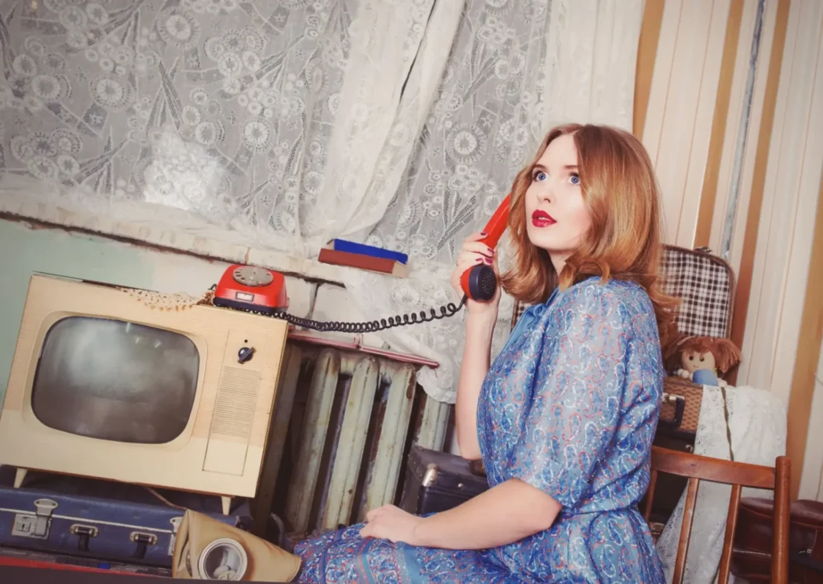mladá žena v retro místnosti telefonuje na starém telefonu, oděná v retro květinových šatech