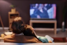 Lidé sedí na gauči a koukají se na televizi.