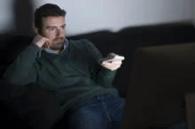muž s vážným výrazem sleduje televizi s ovladačem v ruce