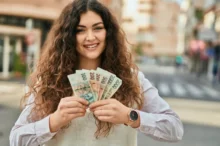 Žena se usmívá a v ruce drží peníze.
