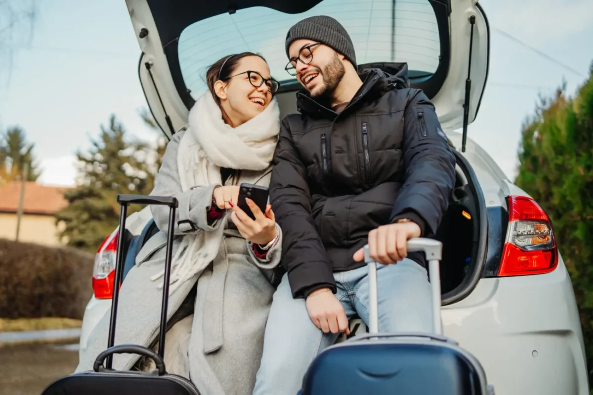 Muž a žena sedí v kufru auta a smějí se.