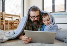 Muž s chlapečkem jsou zachumlaní v dece a koukají se na tablet.