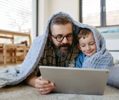 Muž s chlapečkem jsou zachumlaní v dece a koukají se na tablet.