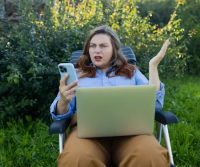 Žena sedí venku a nevěřícně kouká do telefonu.