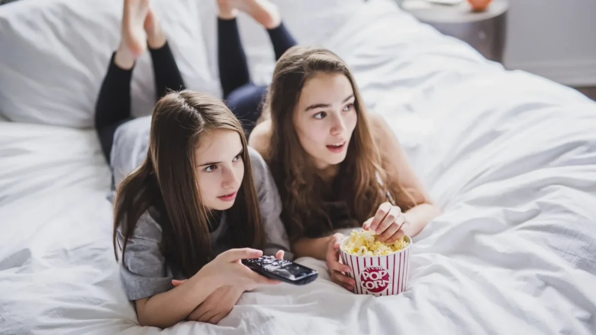 Slečny leží na posteli a mají u sebe popcorn.
