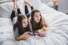 Slečny leží na posteli a mají u sebe popcorn.