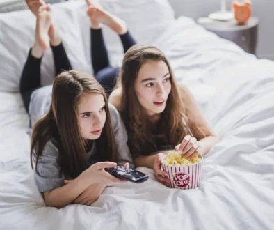 Slečny leží na posteli a mají u sebe popcorn.