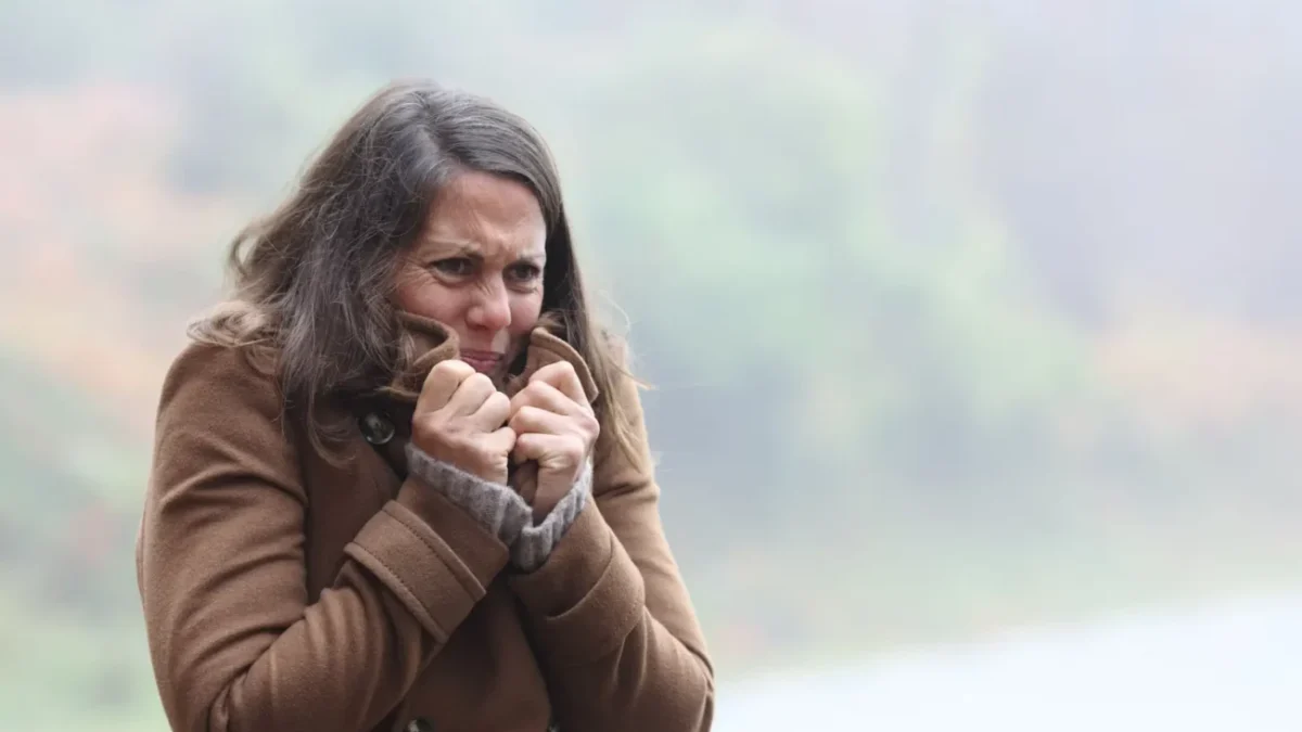 žena v chladném počasí si k tělu přitahuje kabát a tváří se mrzutě