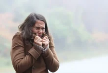 žena v chladném počasí si k tělu přitahuje kabát a tváří se mrzutě