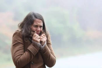 žena v chladném počasí si k tělu přitahuje kabát a tváří se mrzutě