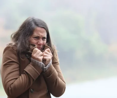žena v chladném počasí si k tělu přitahuje kabát a tváří se mrzutě