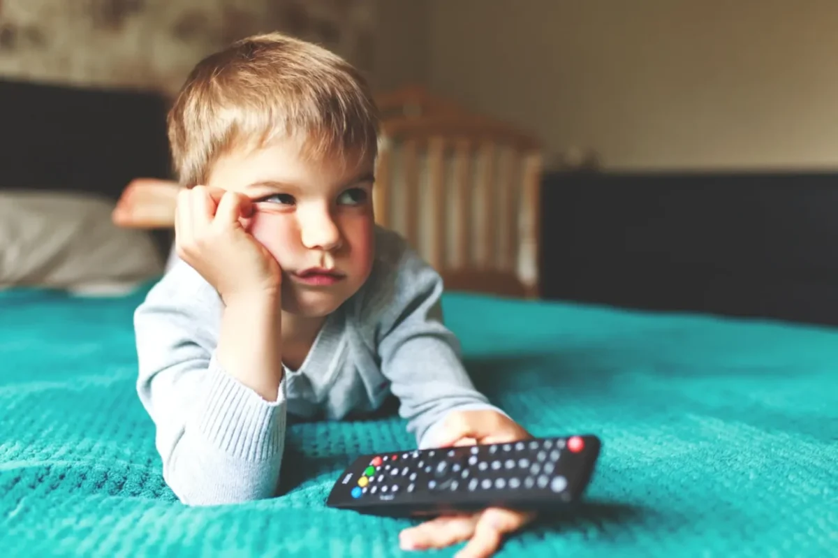 znuděný chlapeček na posteli drží ovladač