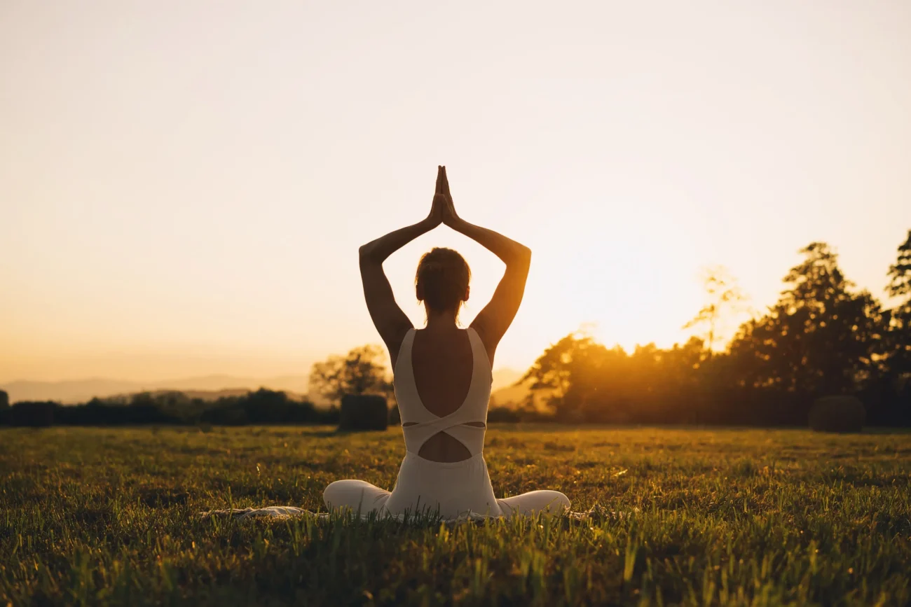 Ke karmické bráně se lze dostat skrz meditace. Zdroj: Shutterstock | TVGURU.cz Žena meditující na louce při západu slunce.