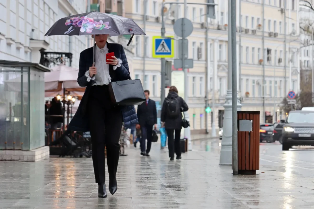 Žena během deště kráčí s deštníkem městem.