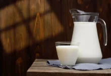 demižon mléka vedle sklenice mléka, oba stojící na dřevěném stole