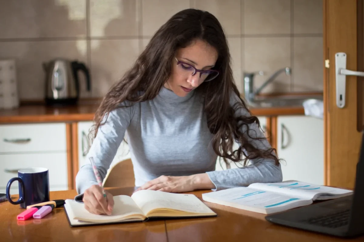 Slečna sedí u stolu a věnuje se studování.