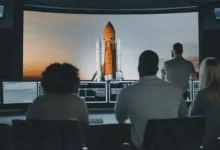 Vývojáři u počítačů a s plátnem s raketou.