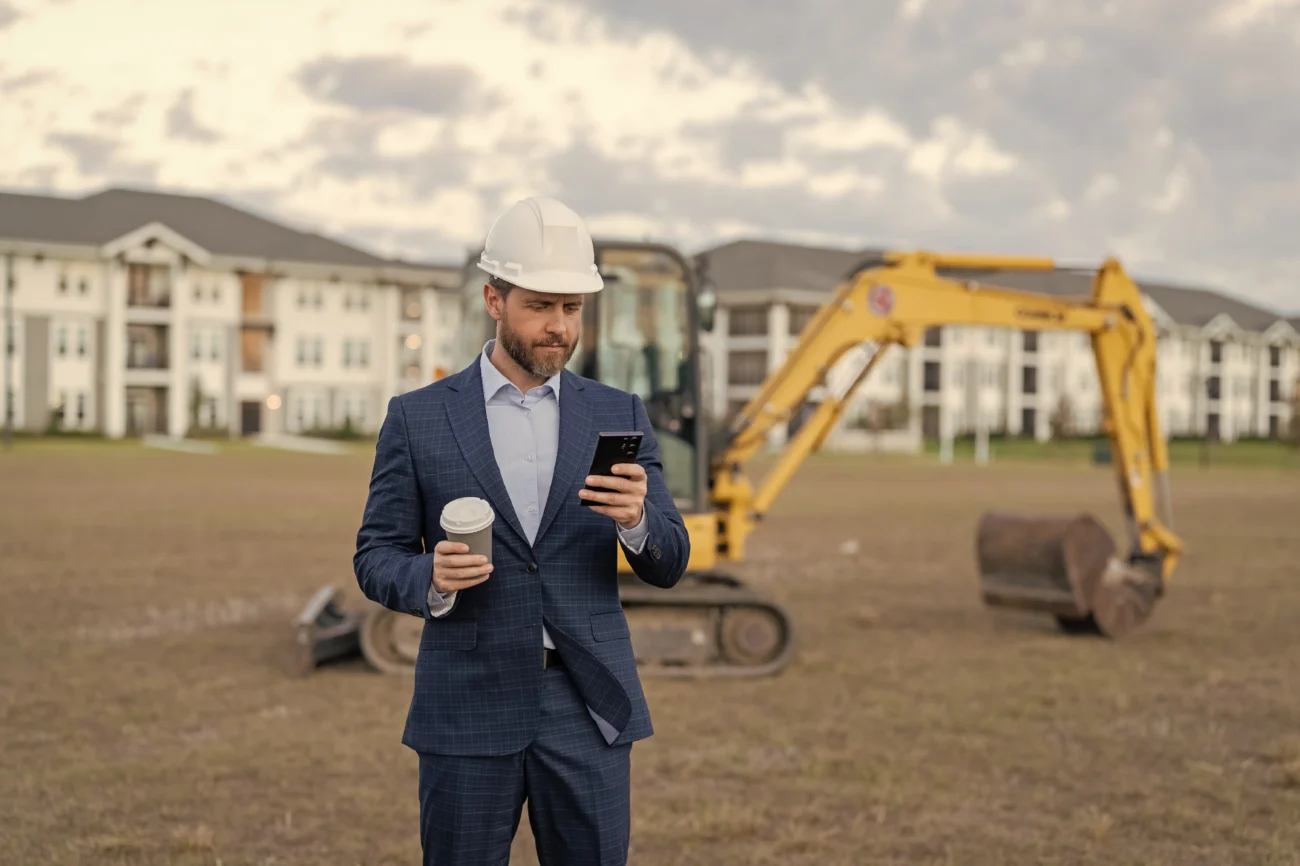 shutterstock_2487436097-2 | TVGURU.cz Muž je na stavbě, v ruce má kávu a kouká do telefonu.