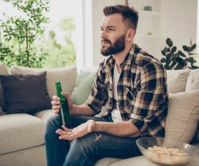 Muž v ruce drží pivo a nechápavě kouká na televizi.