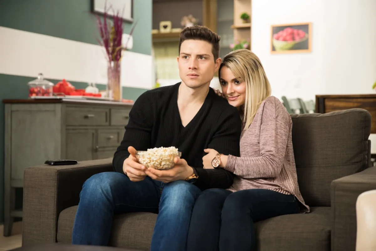 Dva mladí lidé koukají na něco napínavého v televizi.