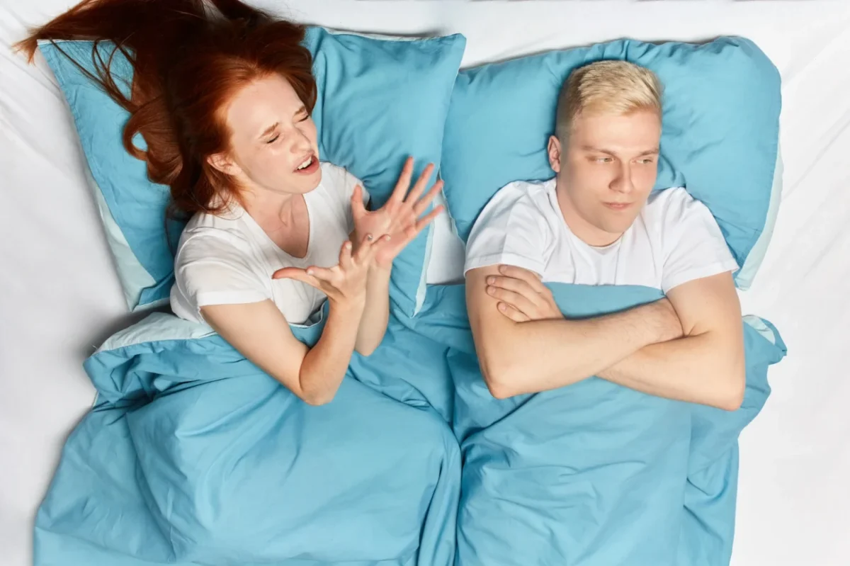 Žena a muž vedle sebe leží naštvaní v posteli.