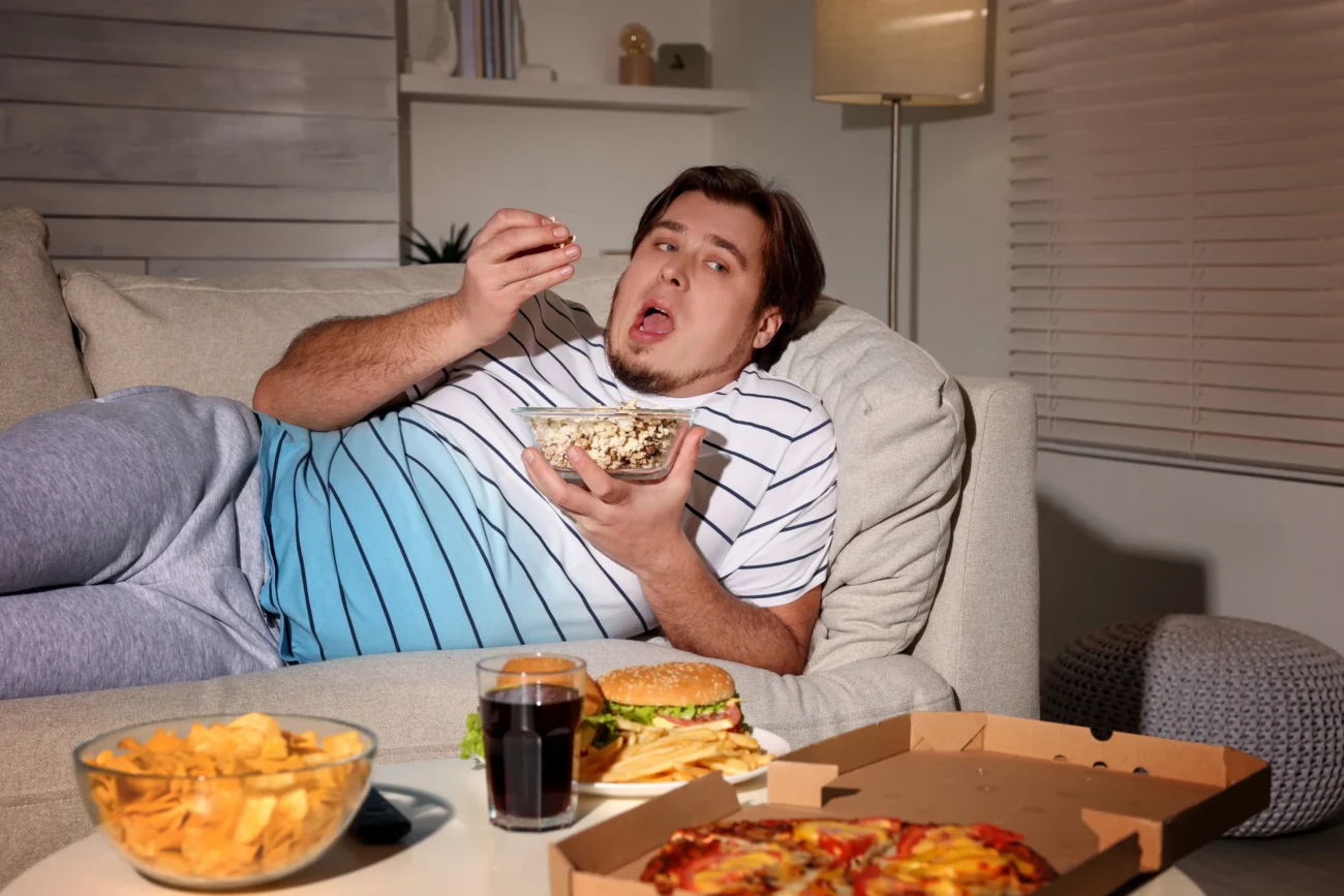 shutterstock_2116394840-2-2 | TVGURU.cz Muž leží na gauči a přejídá se.