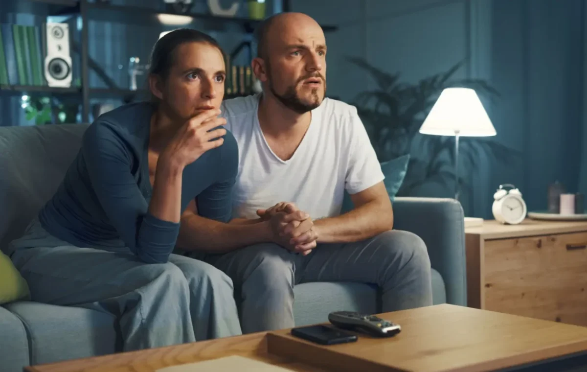 pár na gauči sleduje televizi s překvapeným výrazem