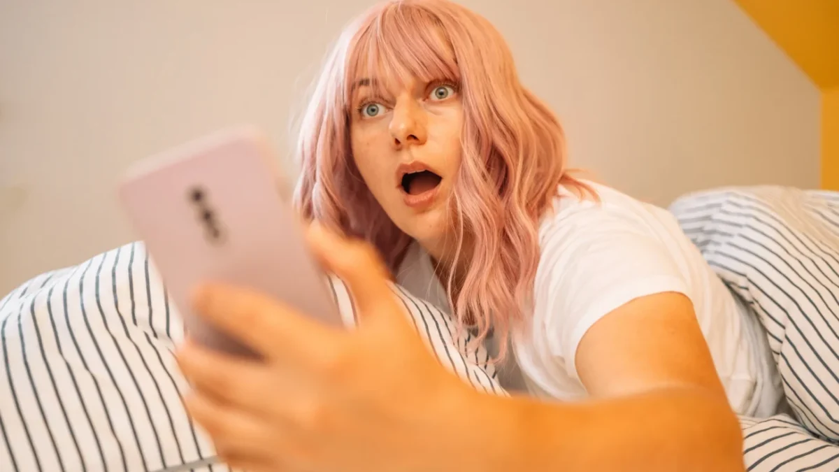Žena zděšeně kouká v posteli do telefonu.