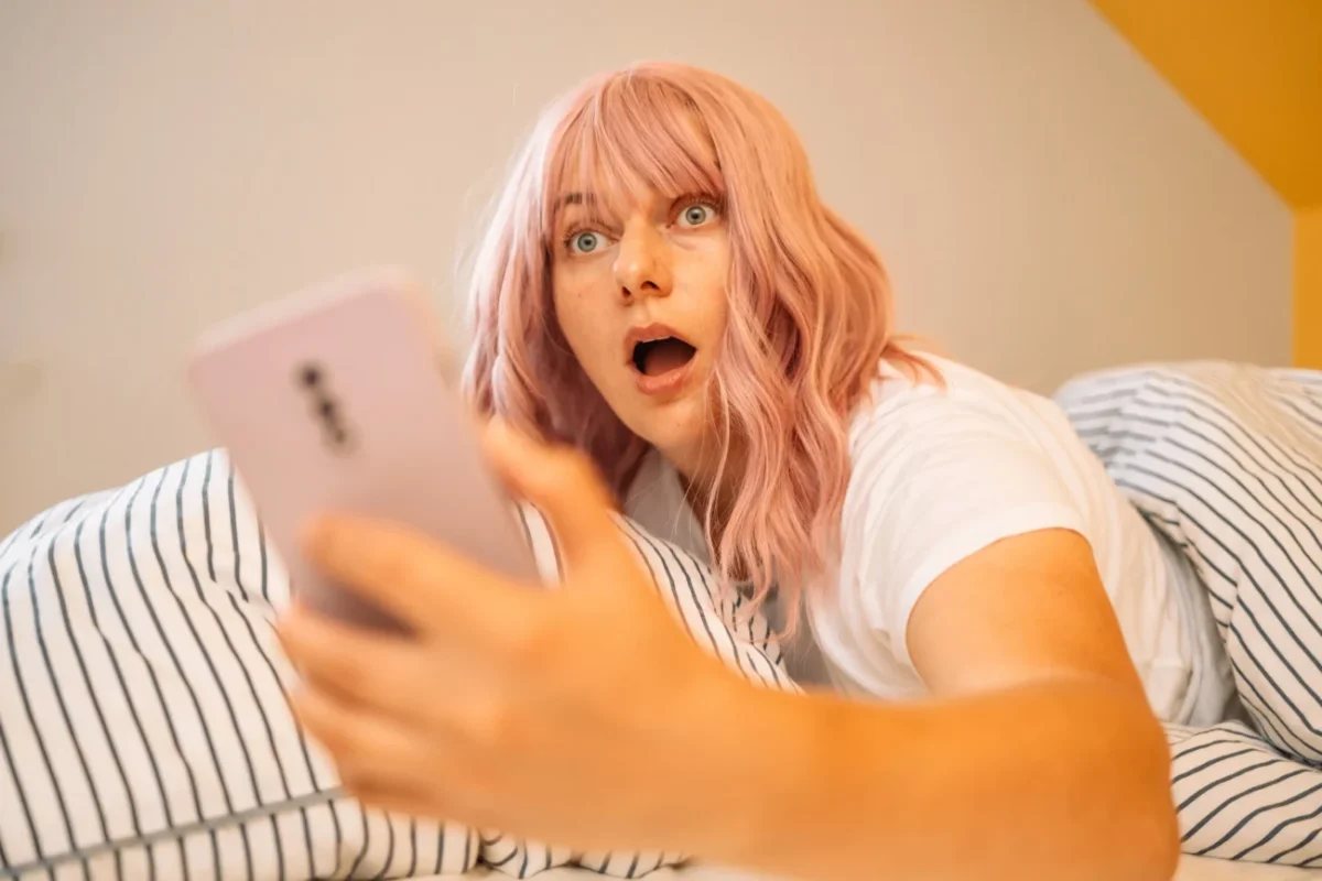 Žena zděšeně kouká v posteli do telefonu.