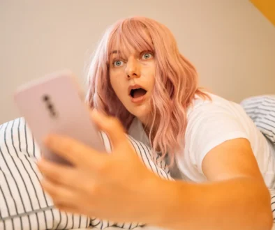 Žena zděšeně kouká v posteli do telefonu.