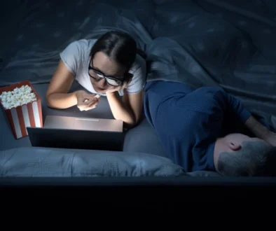 Žena v noci kouká v posteli na film a jí popcorn.