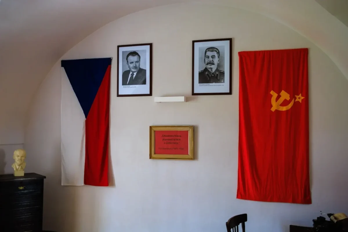 kancelář s československou a sovětskou vlajkou na zdi, kde visí portréty komunistických funkcionářů