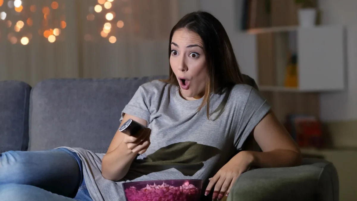 Žena s údivem kouká na televizi a sedí na gauči.
