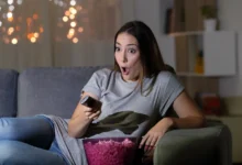 Žena s údivem kouká na televizi a sedí na gauči.