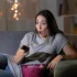 Žena s údivem kouká na televizi a sedí na gauči.