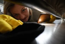 Žena si mobilem svítí pod gauč a něco hledá.