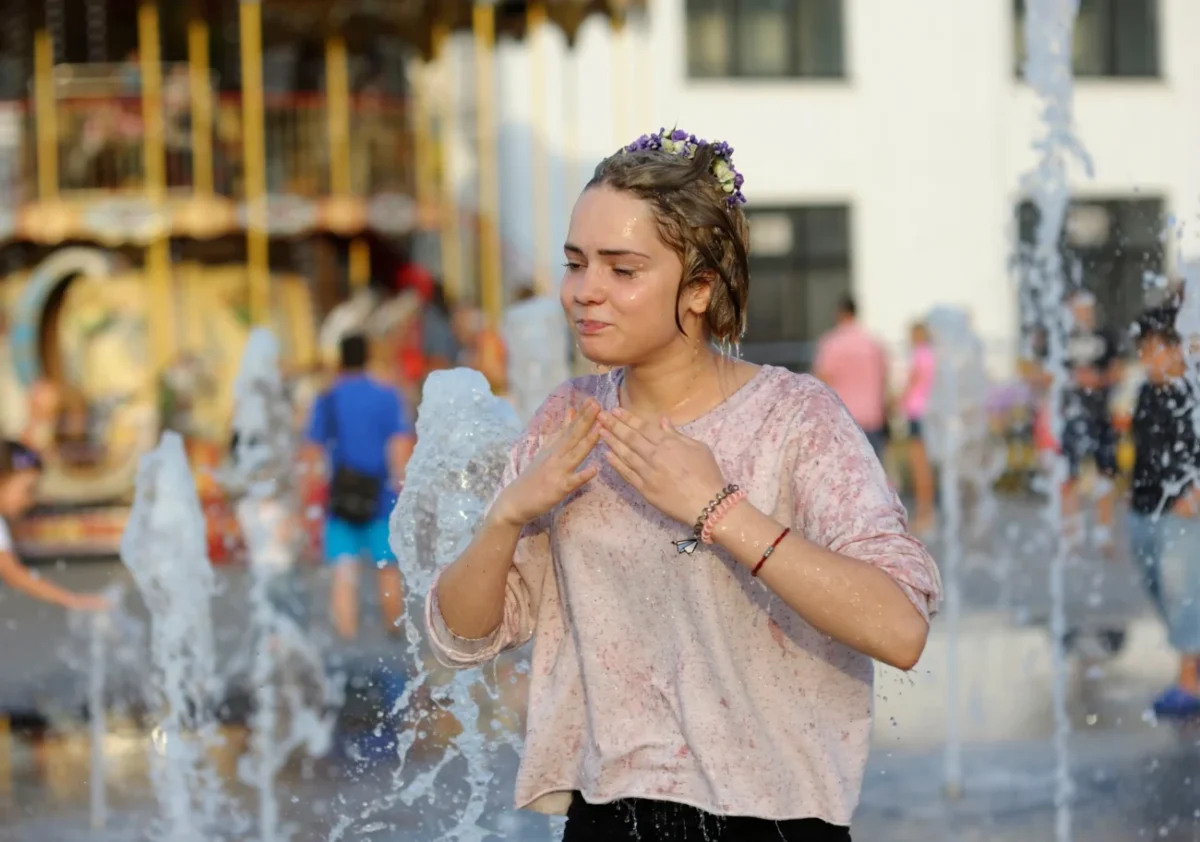 Holčička je zlitá vodou a stojí před fontánou.