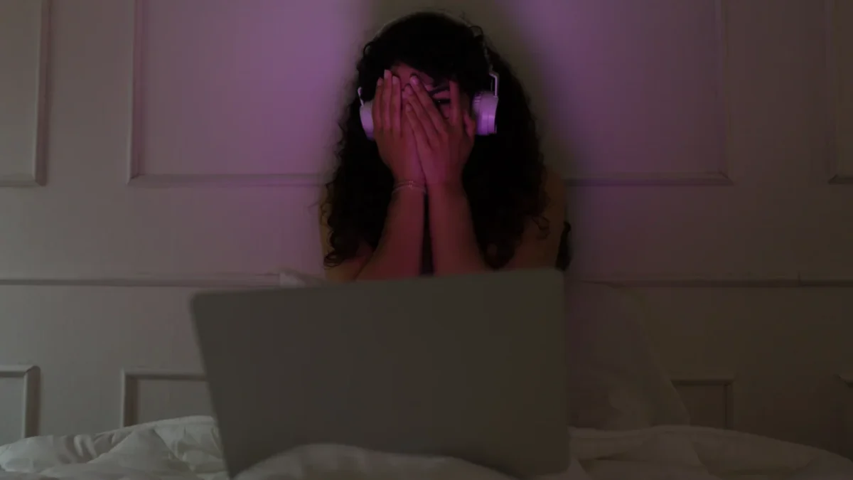 Žena sedí u notebooku a vystrašeně si zakrývá oči.